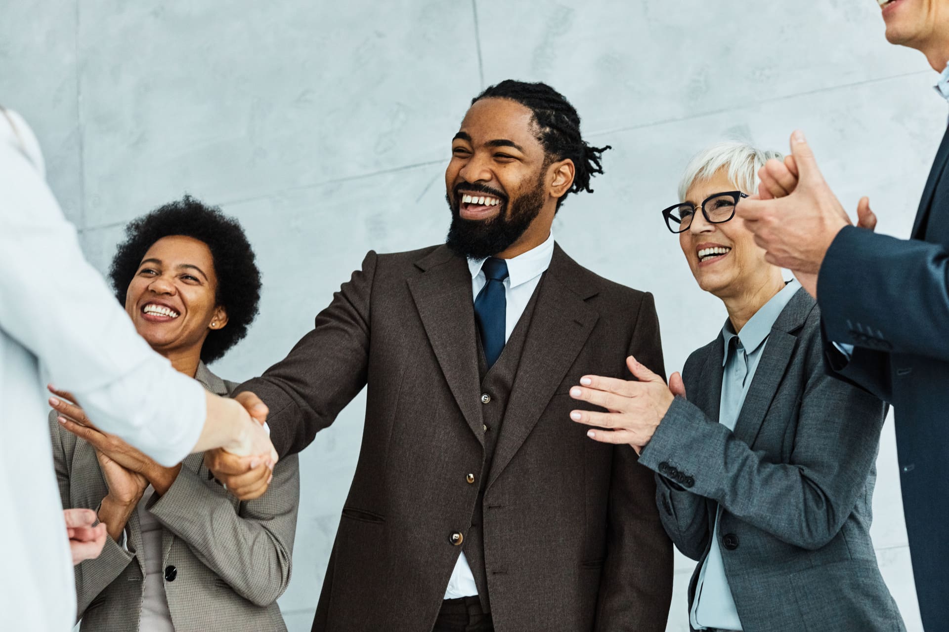 Business professionals shaking hands and smiling while colleagues applaud