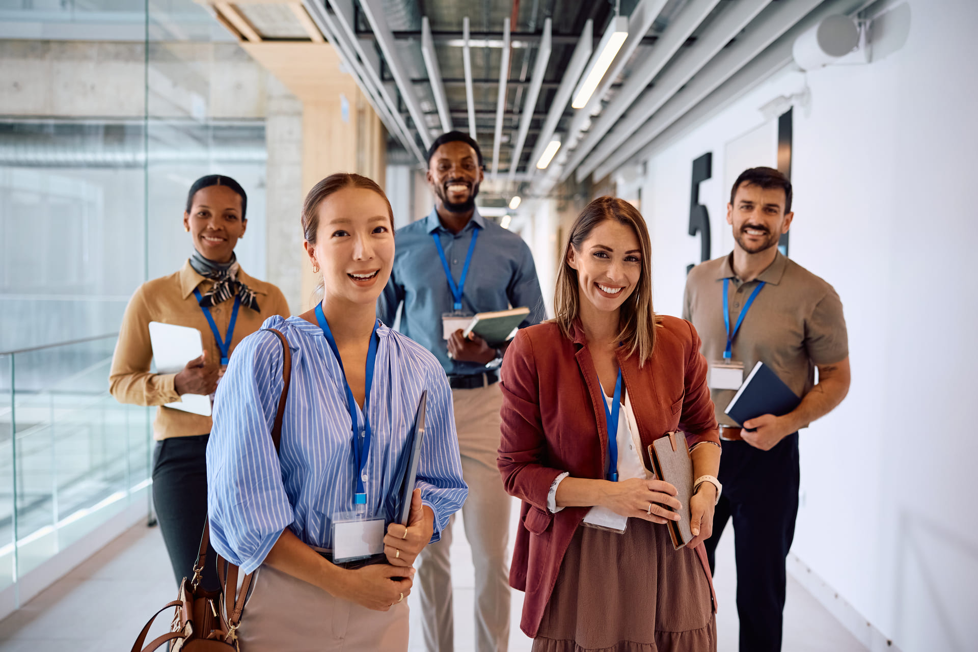 Group of diverse professionals walking in a corporate hallway, wearing lanyards and holding notebooks