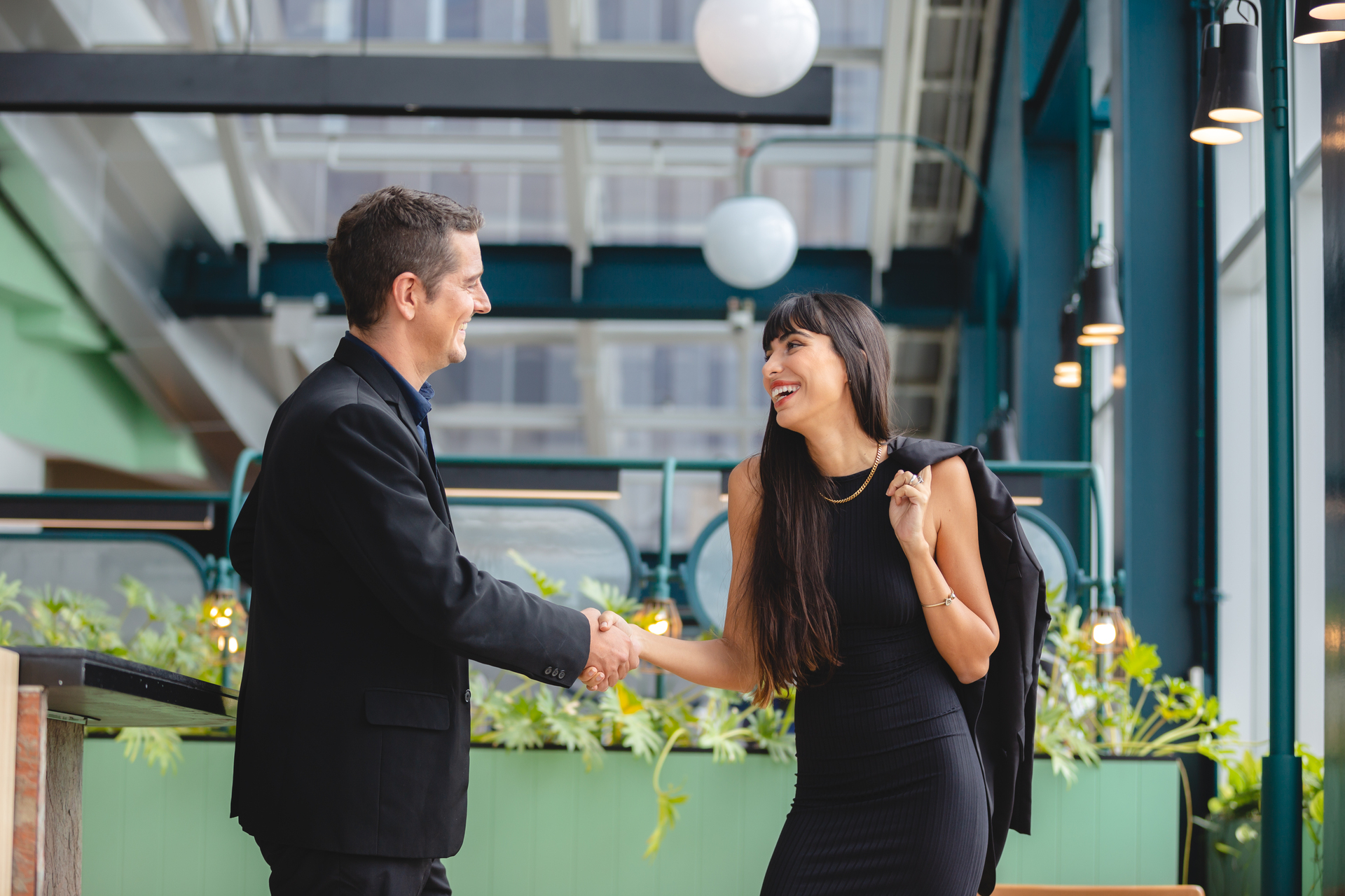 Professional-man-and-woman-greeting-each-other-with-a-handshake-in-a-modern-office-atrium-both-smiling-and-dressed-in-business-attire
