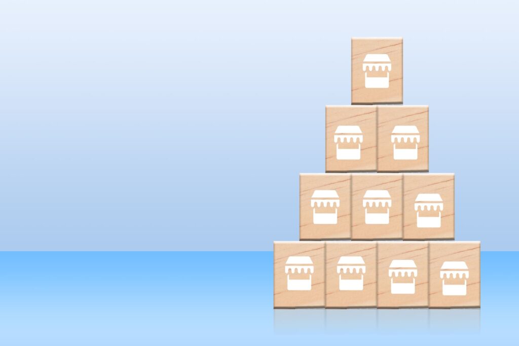 Pyramid of wooden blocks with store icons showing franchise expansion