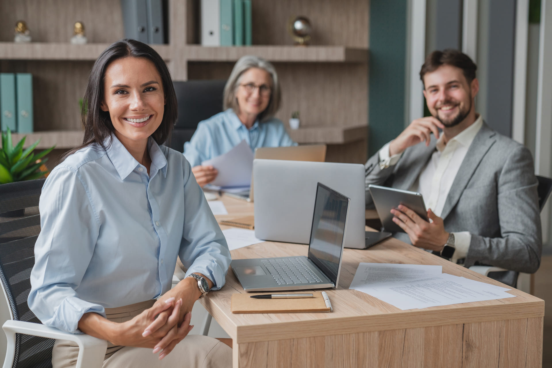 Team of professionals in a modern office, smiling while working on laptops and tablets