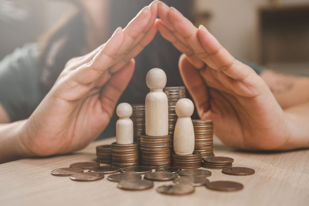 Hands protecting wooden family figures with stacked coins