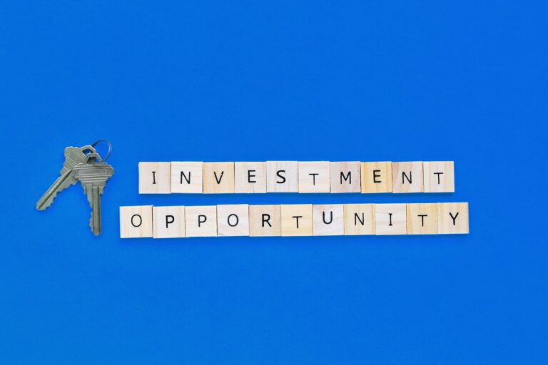 Wooden blocks spelling “Investment Opportunity” with house keys on blue background