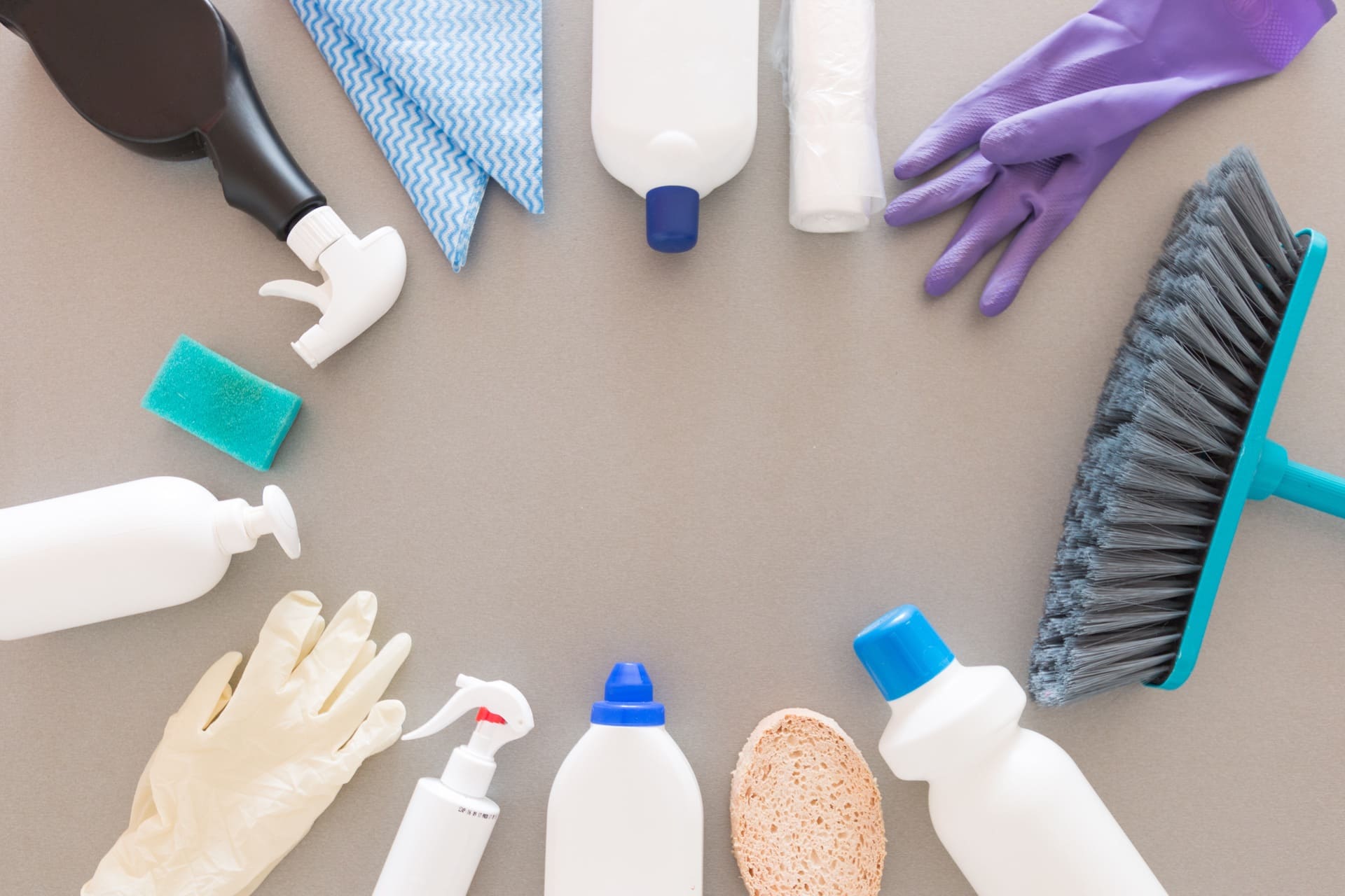 Top view of cleaning products, gloves, sponge, and broom arranged in a circle