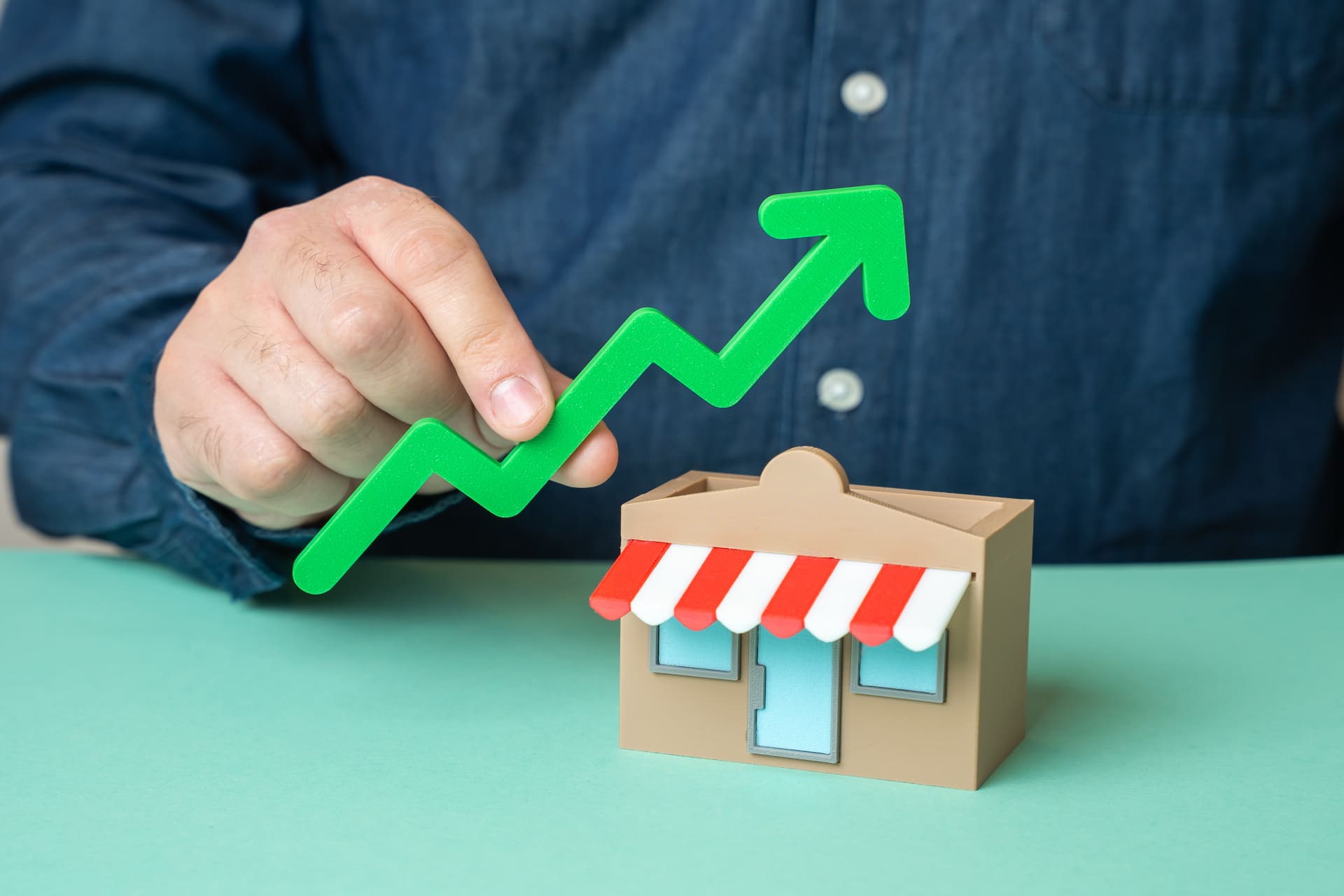 a-man-holds-a-green-arrow-pointing-up-over-a-store
