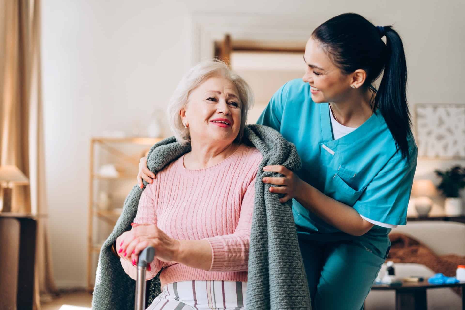 Caregiver placing a warm blanket around an elderly woman