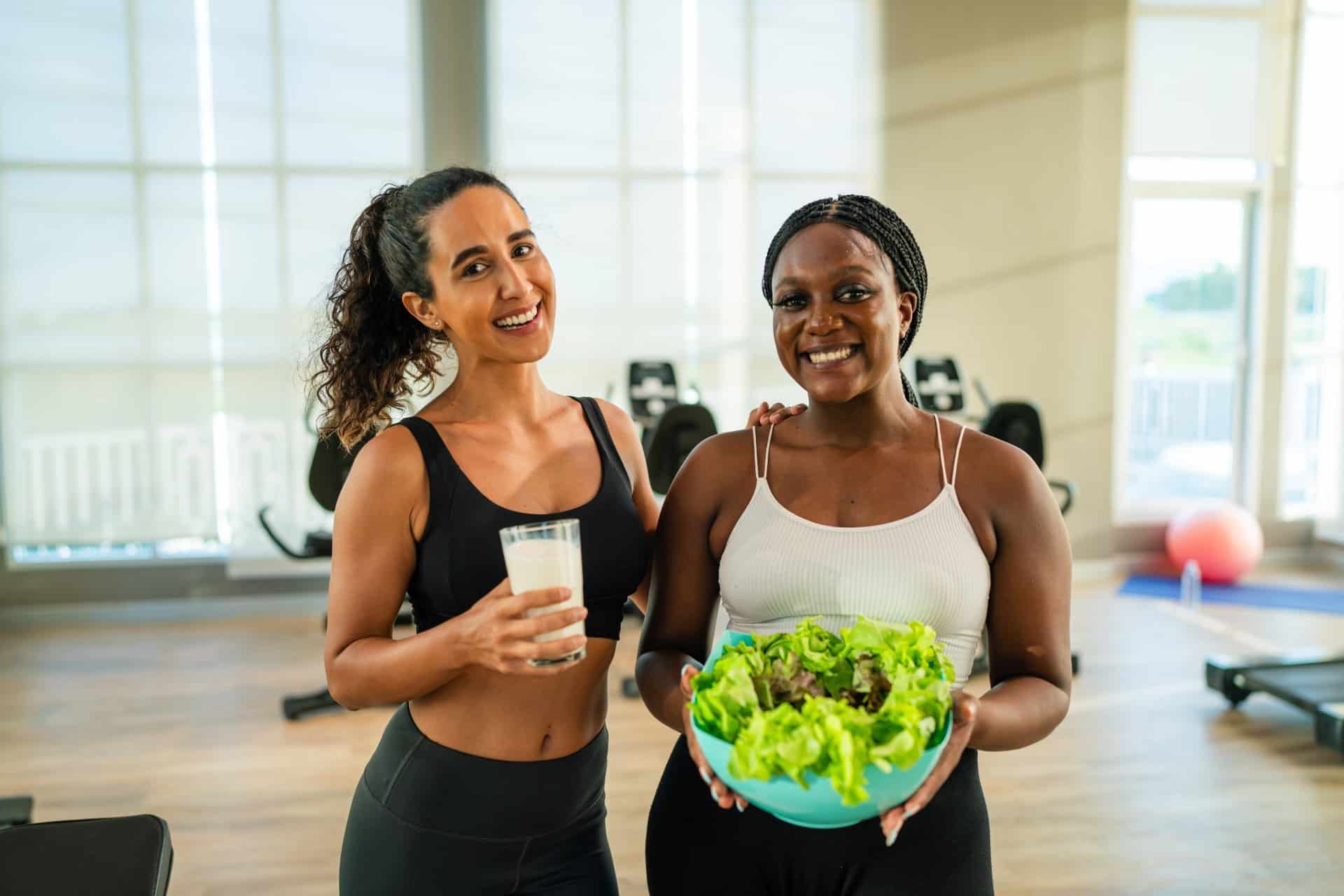Two women holding healthy food and drinks at the gym